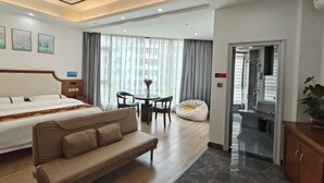 Habitación de hotel con cama, sofá, mesa de comedor con sillas, un sillón informal y vistas al exterior.