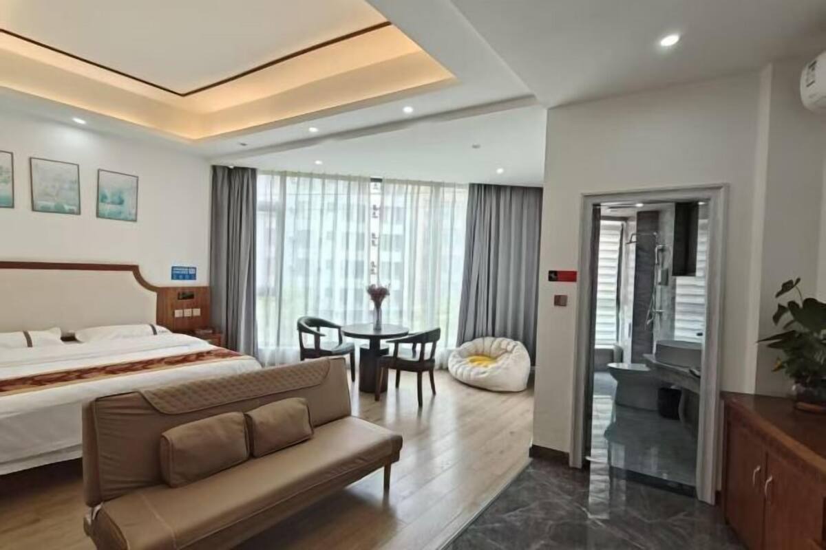 A hotel room with a bed, a sofa, a dining table with chairs, a bean bag, and a view of the outdoors.