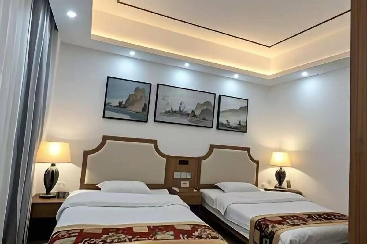 A hotel room with two beds, a wooden headboard, bedside lamps, and three framed artworks on the wall.