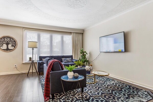 A modern living room with a dark blue sofa, a patterned rug, a round coffee table, and a TV mounted on the wall. - Cosy Spacious 3+2 bedroom house , one bus to subway station (Toronto)