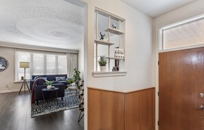 Un salon avec un canapé bleu foncé, une petite table ronde et un tapis à motifs. On y trouve une bibliothèque avec des objets décoratifs et un panneau accroché au mur.