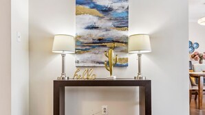 A modern living room with a dark wood console table, two wall-mounted lamps, a 'hello' sign, and a large abstract painting. - Cosy Spacious 3+2 bedroom house , one bus to subway station (Toronto)