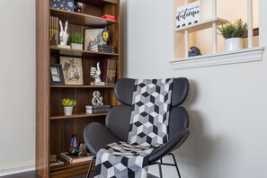 A modern living room with a black leather armchair, a wooden bookshelf with various decorative items, and a white shelf with a welcome sign.
