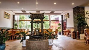 En rymlig lobby med en traditionell asiatisk vattenfontän, möbler i trä och stora fönster som ger utsikt över den omgivande grönskan.
