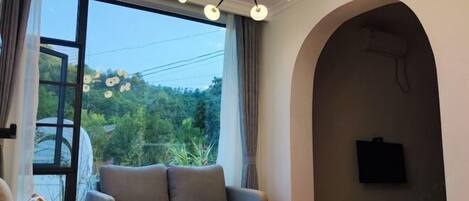A living room with a sofa, a round table, a chandelier, and a television mounted on the wall.