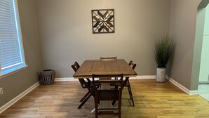 Ein Esszimmer mit Holztisch und Stühlen, einer Topfpflanze und einem geometrischen Wandbild.