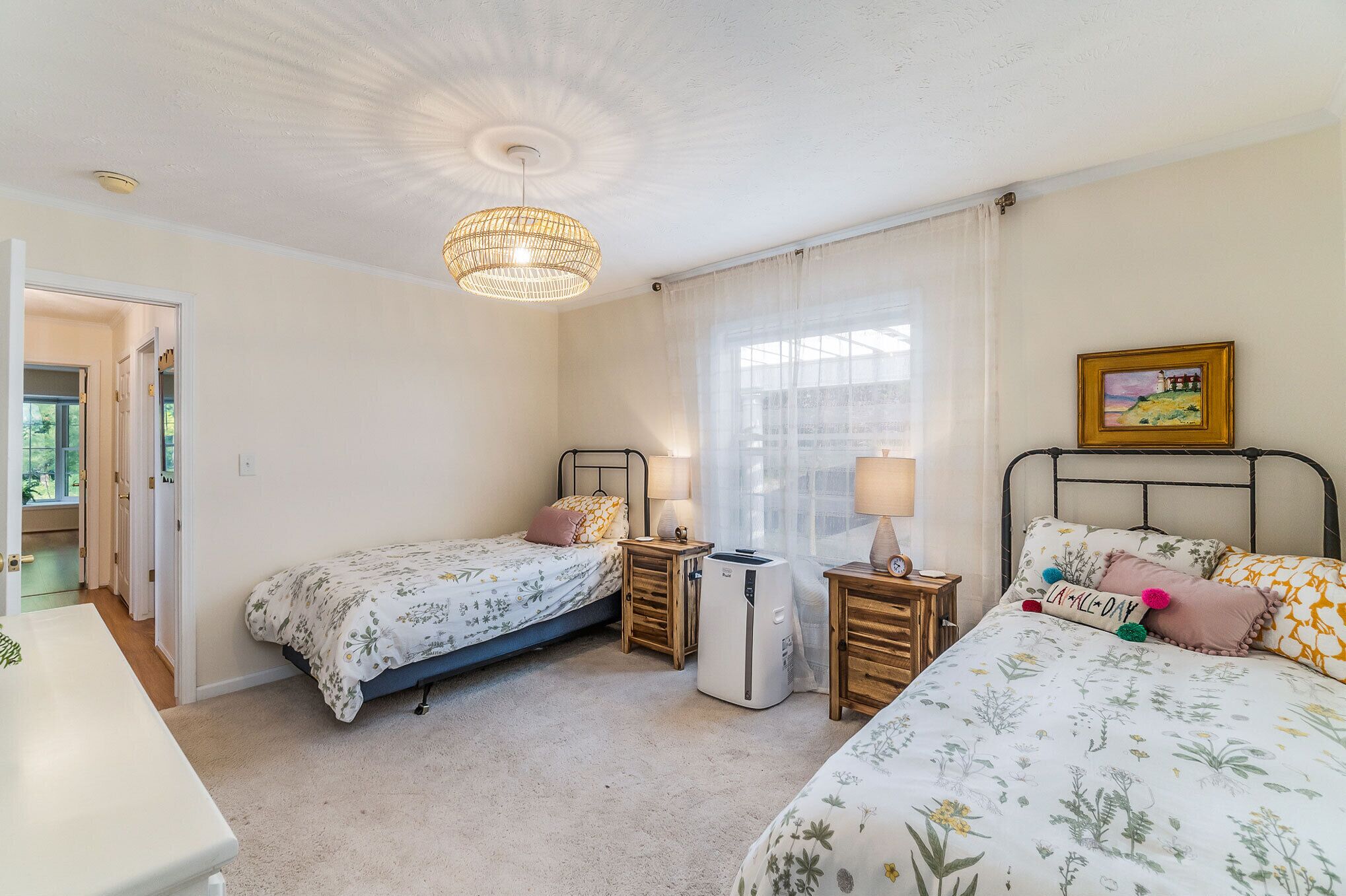 A bedroom with two single beds, a bedside table with a lamp, a heater, and a window with curtains.