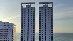 A high-rise building with a central courtyard, surrounded by parking and greenery, overlooking a body of water.
