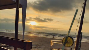 A beachside table with a drink and umbrella, overlooking the ocean and a sunset.