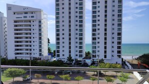 A balcony with a view of tall residential buildings, a parking area, and a beach.