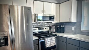 A modern kitchen with stainless steel appliances, white cabinets, a microwave, a coffee maker, and a water dispenser.