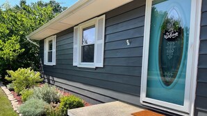 A house with a dark siding exterior, a welcome sign on the front door, and a small garden with various plants.