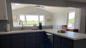 A modern kitchen with dark cabinets, a dishwasher, and a window overlooking a garden.
