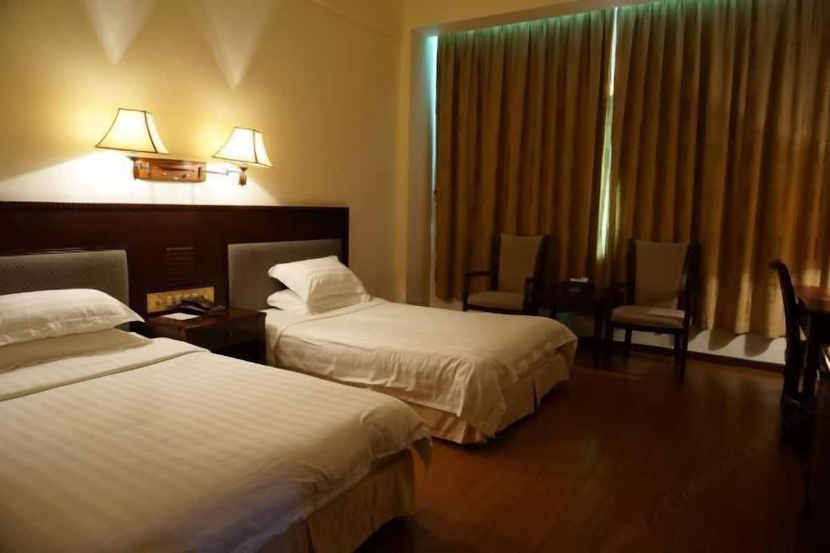 Habitación de hotel con dos camas individuales, una mesita de noche, una silla y un gran ventanal con cortinas.