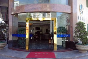 Entrada de un hotel con puerta de cristal, alfombra roja y plantas en macetas.