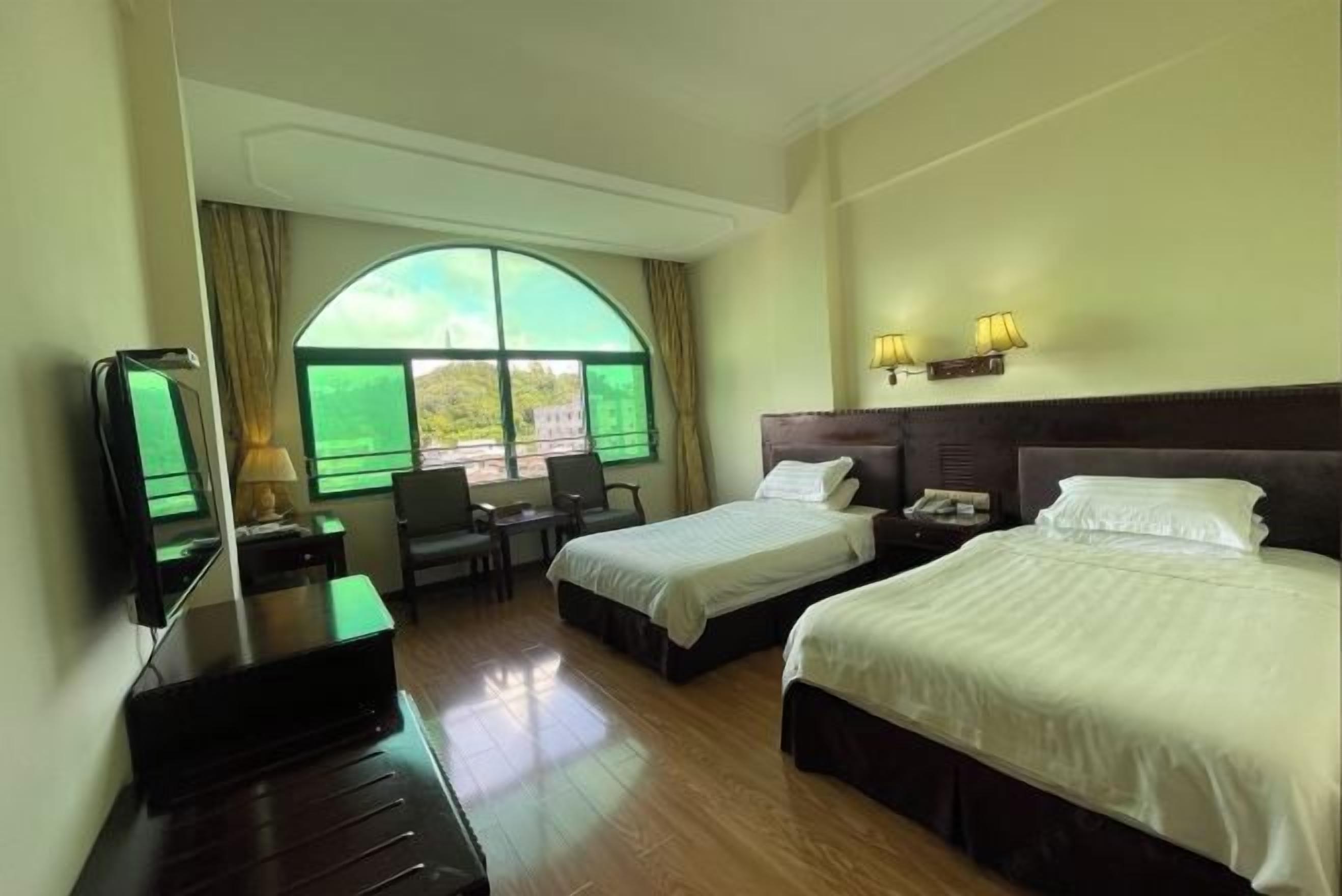 A hotel room with two beds, a desk, a chair, a TV, and a large window with curtains.