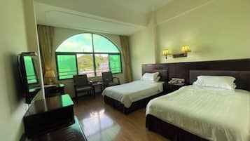 A hotel room with two beds, a desk, a chair, a TV, and a large window with curtains.