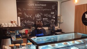 A café with a chalkboard menu, a display case with pastries and drinks, and a barista preparing coffee. - Lastarria Hotel (Santiago)