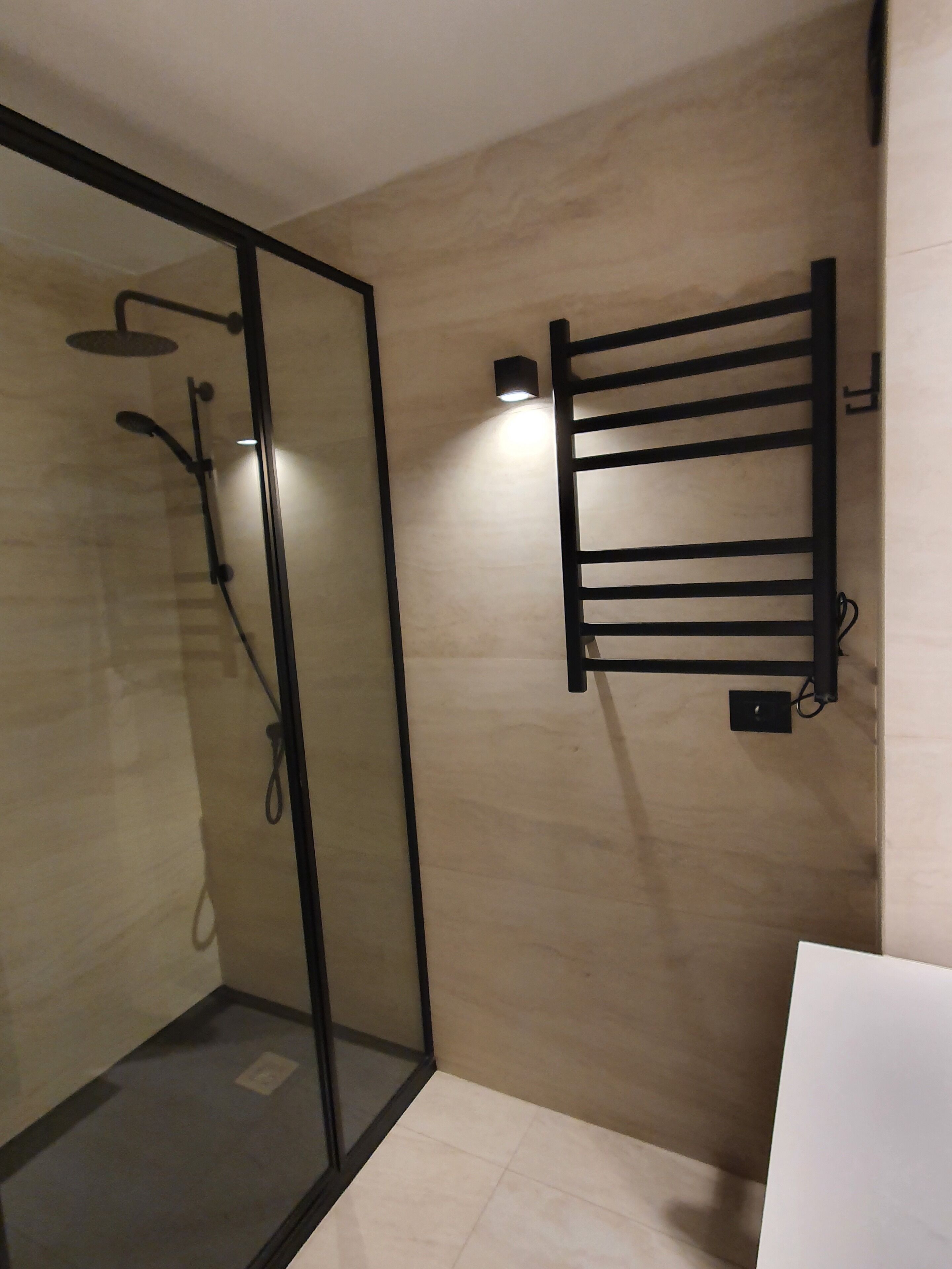 A modern bathroom with a glass shower enclosure, a towel rack, and a white sink.