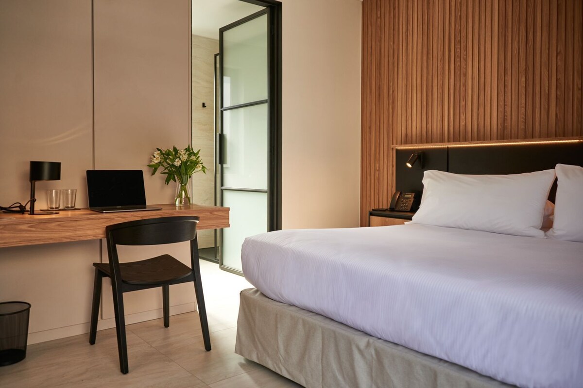 A modern hotel room with a bed, desk, chair, and a small plant.