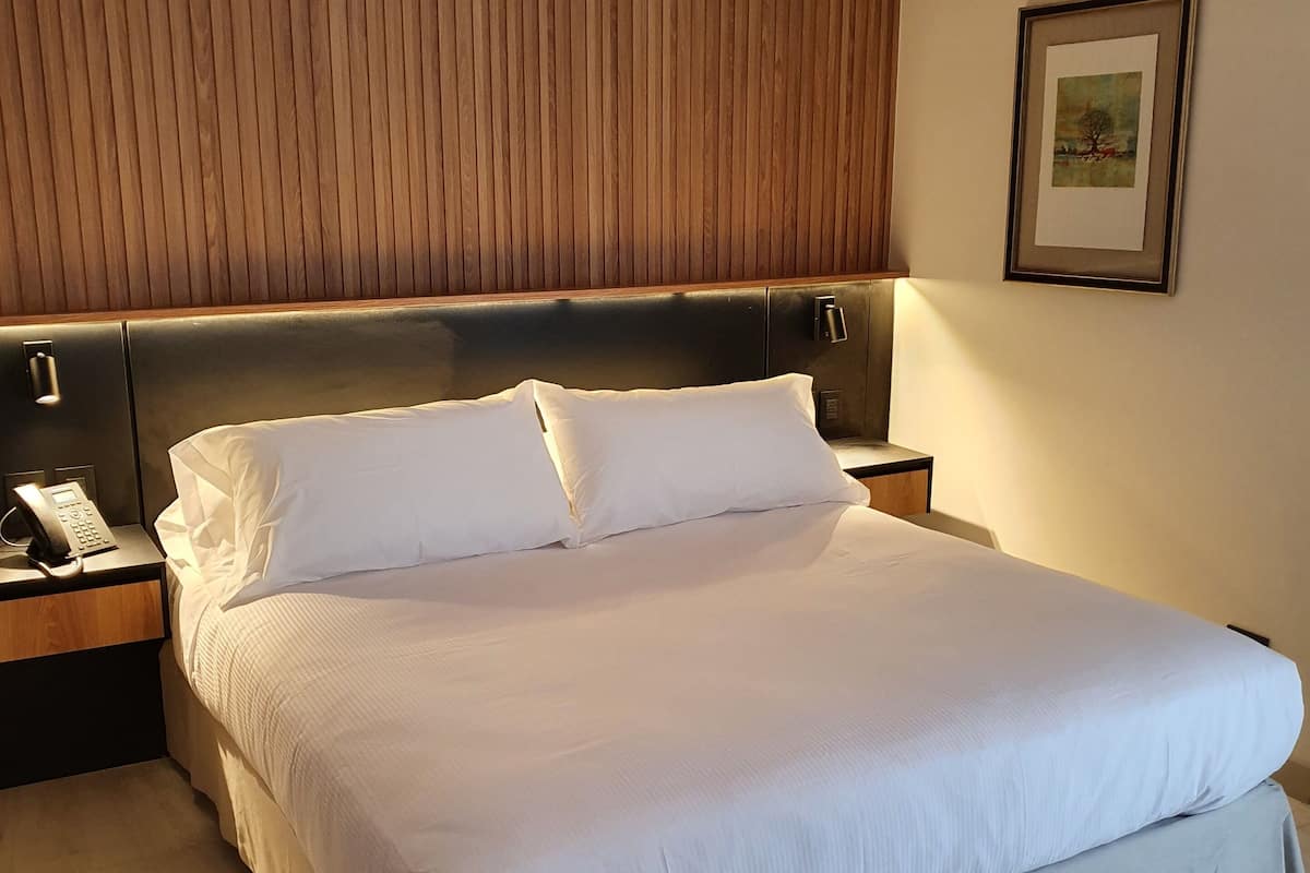A neatly made bed with white linens, a wooden headboard, and a bedside phone on a nightstand.