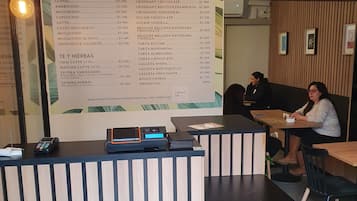Kahvila, jossa on puinen vastaanottotiski, ruokalista ja kaksi ihmistä istumassa pöydän ääressä.