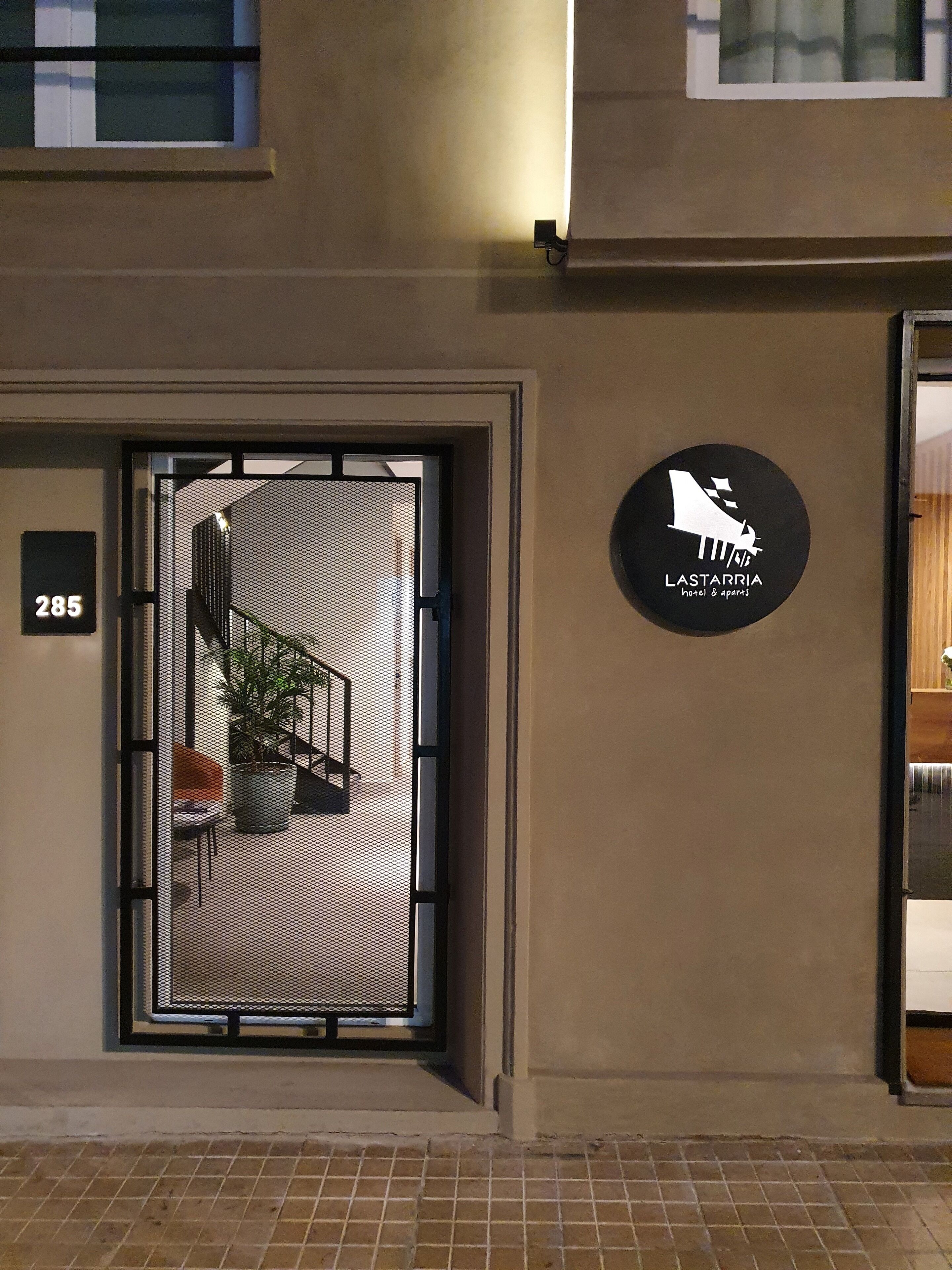 A hotel entrance with a metal gate, a potted plant, and a sign indicating the hotel name and amenities.