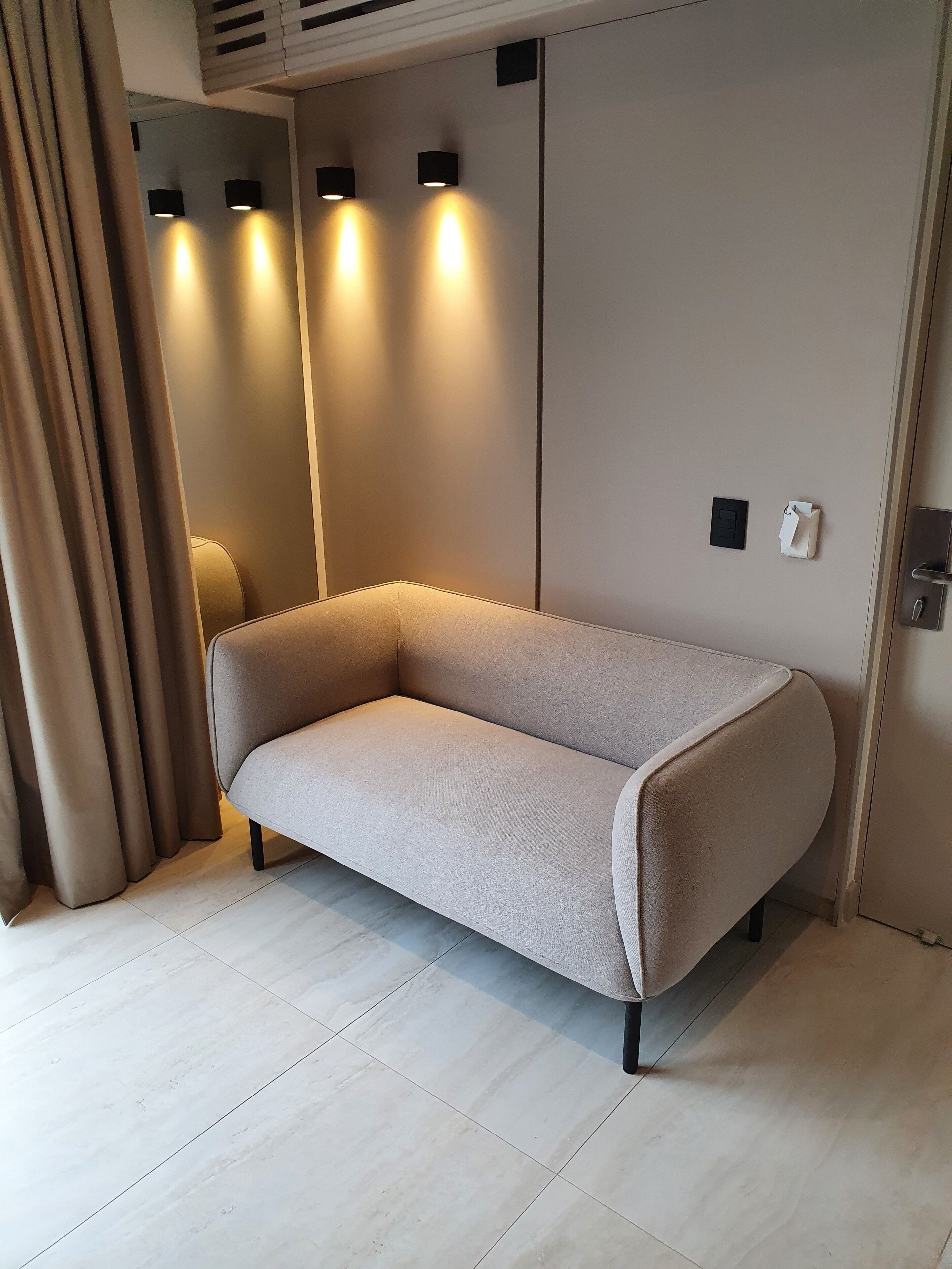 A modern room with a beige sofa, a light-colored floor, and wall-mounted lights.