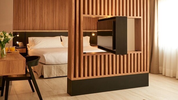 A modern hotel room with a wooden partition, a bed, a TV, a desk with a chair, and a dining table with a vase of flowers. - Lastarria Hotel (Santiago)