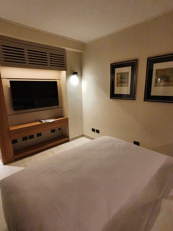 Habitación de hotel con una cama grande, un televisor de pantalla plana montado en un mueble de madera y dos cuadros enmarcados en la pared.