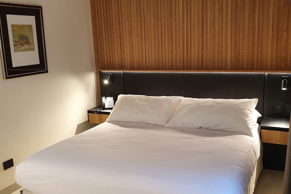 A neatly made bed with white linens, a wooden headboard, and a bedside table with a lamp.