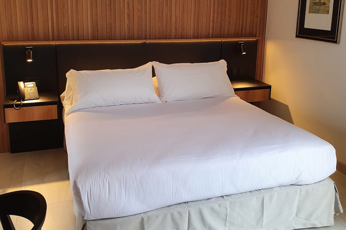 A neatly made bed with white linens, a wooden headboard, and two bedside tables with lamps.