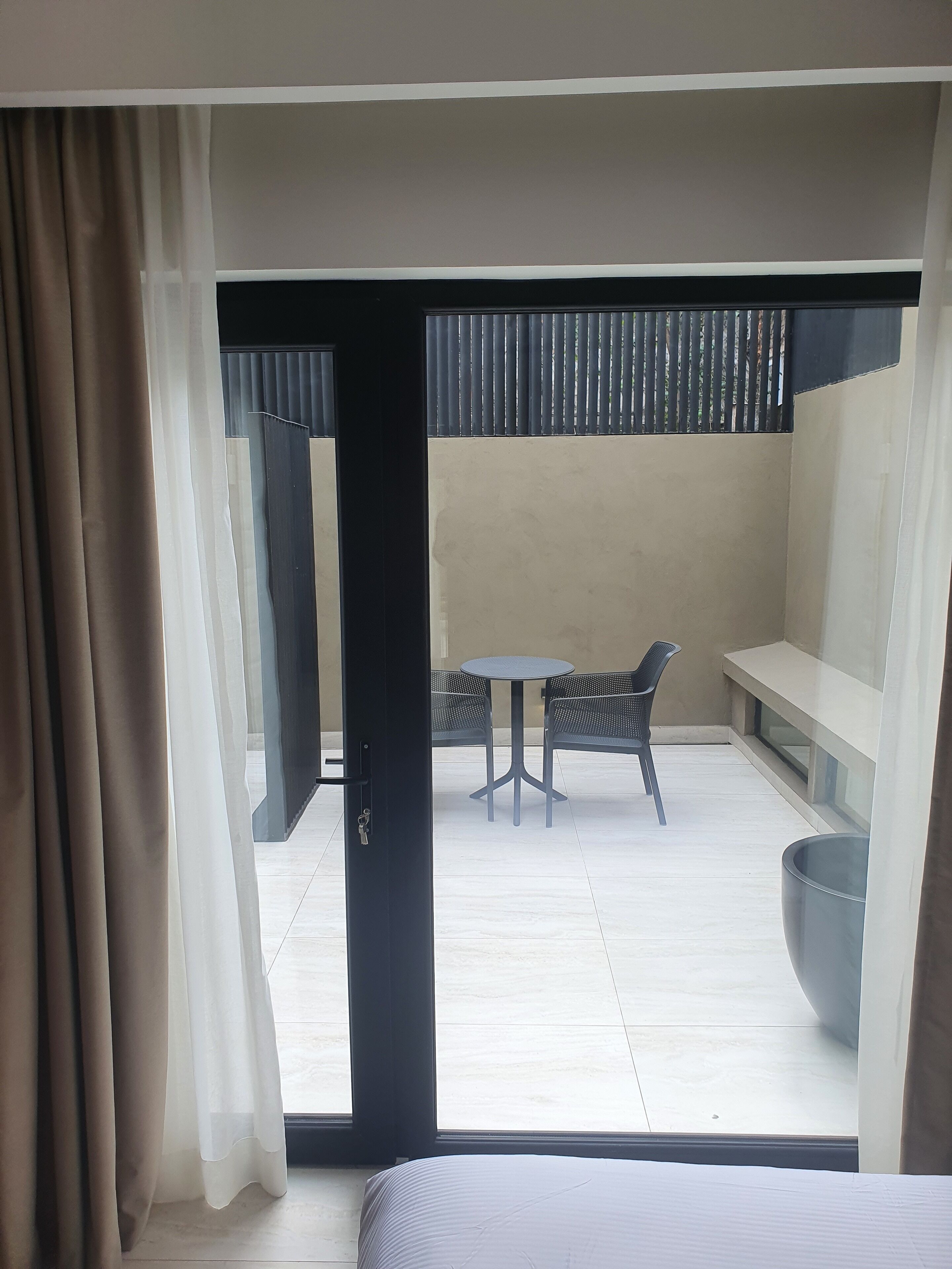 A modern room with a bed, a balcony with a table and chairs, and a large window with curtains.