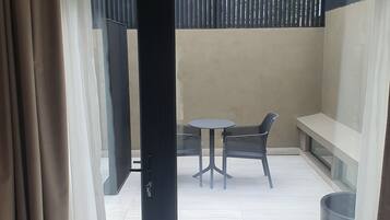 A modern room with a bed, a balcony with a table and chairs, and a large window with curtains.