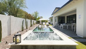 Una piscina con fuente acuática, rodeada por un patio con mobiliario exterior y una zona de estar cubierta.
