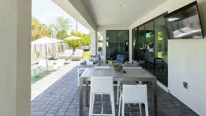 Un patio moderno al aire libre con piscina, mobiliario blanco y zona de comedor.