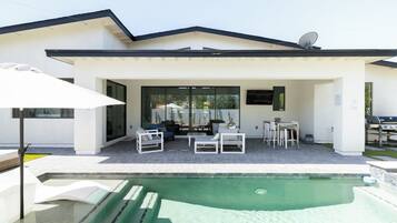 A modern house with a covered patio, outdoor seating, and a swimming pool.