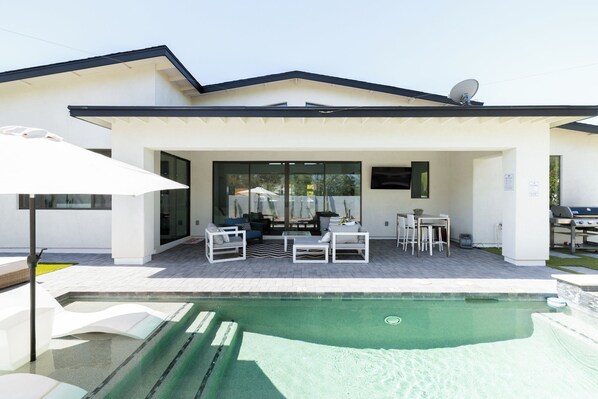 Una casa moderna con patio coperto, area relax all'aperto e piscina.