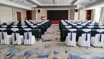 A conference room with rows of tables and chairs, a stage, and a carpeted floor.