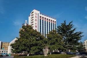 Un edificio de varios pisos con un letrero llamativo, rodeado de árboles y otros edificios.