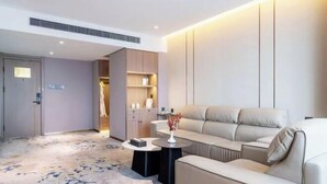 A modern hotel room with a sofa, a small coffee table, and a side table. There is a wardrobe with a mirror and a door leading to another room. - Kunyu Hotel (Weihai)