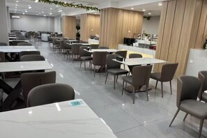 A modern dining area with multiple tables and chairs, a counter, and a clean, tiled floor. - Kunyu Hotel (Weihai)