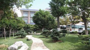A pathway through a landscaped garden with trees and shrubs, leading to a building with a blue roof.