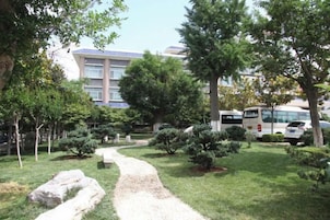 A pathway through a landscaped garden with trees and shrubs, leading to a building with a blue roof.
