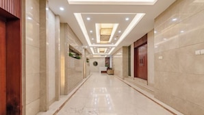 A hotel corridor with a marble floor, wooden doors, and recessed lighting. - Kunyu Hotel (Weihai)