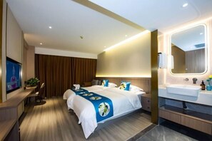 Una habitación de hotel moderna con una cama grande, un escritorio, un televisor y un baño con espejo y lavamanos.