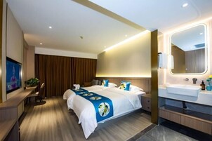 Una habitación de hotel moderna con una cama grande, un escritorio, un televisor y un baño con espejo y lavamanos.