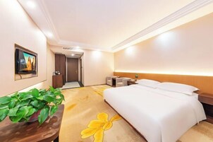 Una habitación de hotel con una cama, una mesita de noche, un televisor y una planta.