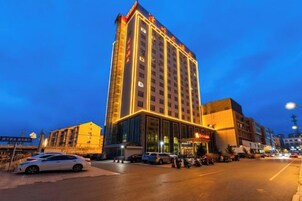 Un hotel de varios pisos con una entrada destacada y un estacionamiento frente al edificio.
