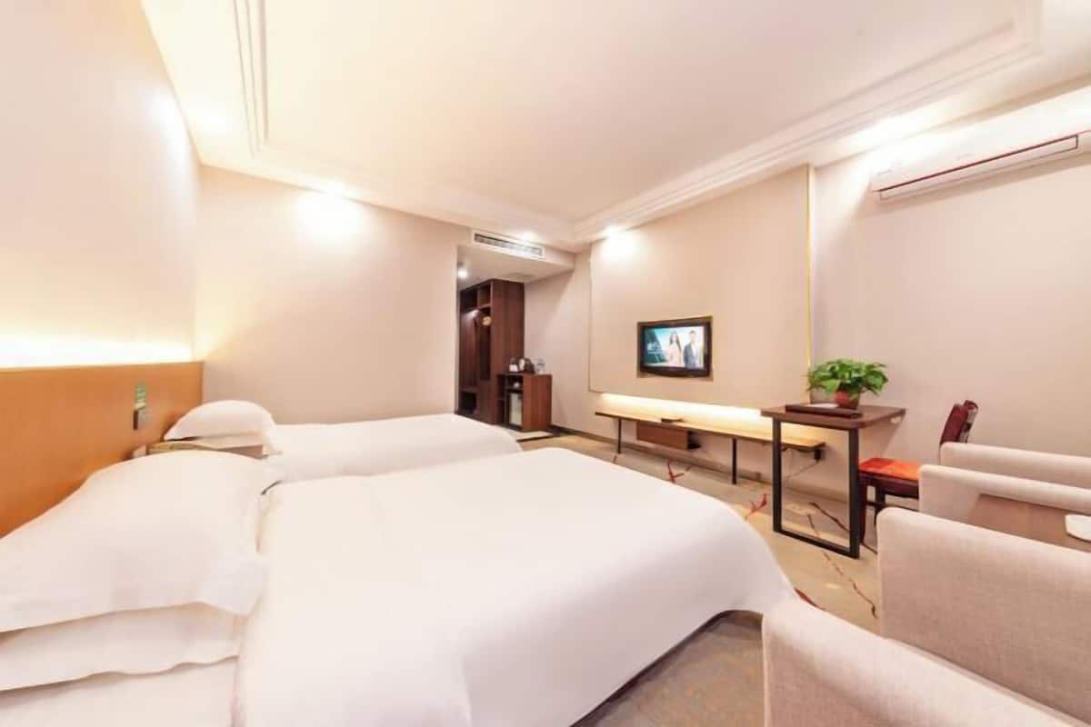 A hotel room with two beds, a desk, a chair, a television, and a small table with a plant.